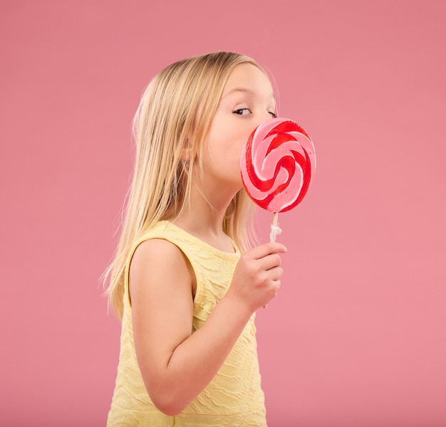 Doces doces e pirulito com garota no estúdio para festa de açúcar e comida de carnaval isolada em fundo rosa Bonito positivo e jovem com criança e comendo lanche colorido para brincadeiras e guloseimas