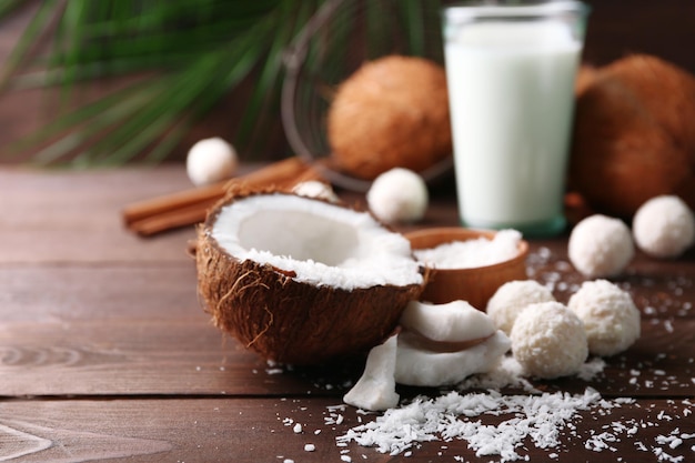 Doces em flocos de coco, copo de leite e coco fresco em fundo escuro de madeira