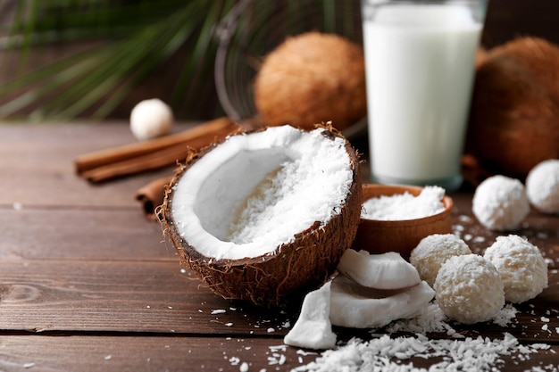 Doces em flocos de coco, copo de leite e coco fresco em fundo escuro de madeira