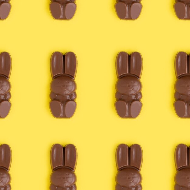 Doces em forma de coelhinho da Páscoa de chocolate ao leite, deitado em fileiras no fundo amareloComposição de feriado religiosoPadrão de coelho para cartão de felicitaçõesSímbolo de celebração Domingo de Cristo