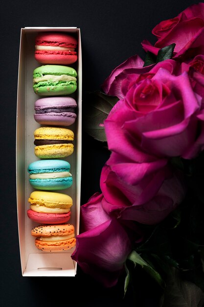 Doces macaroons coloridos e rosas em fundo preto