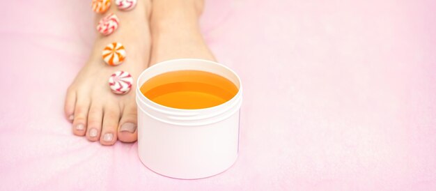 Doces redondos em uma fileira nos pés femininos com o frasco branco com pasta de açúcar no fundo rosa com espaço de cópia, o conceito de depilação.