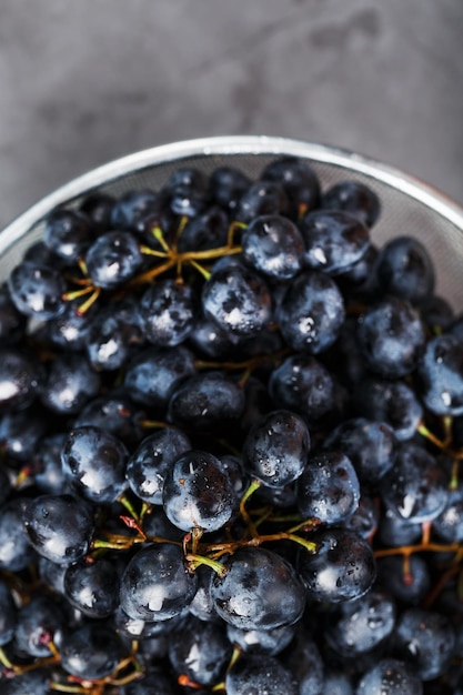 Doces uvas pretas em uma tigela de metal em um fundo escuro e texturizado. vista do topo