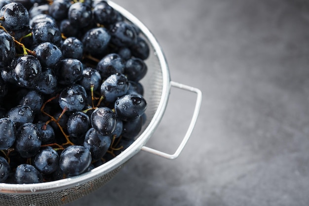 Doces uvas pretas em uma tigela de metal em um fundo escuro e texturizado.