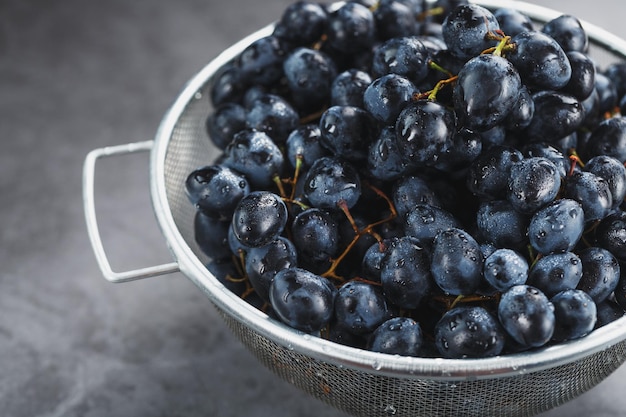 Doces uvas pretas em uma tigela de metal em um fundo escuro e texturizado.