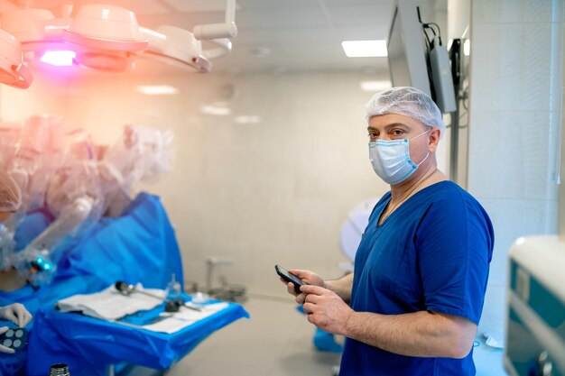 Docktor adulto en quirófano. Hombre en uniforme sosteniendo teléfono en quirófano en hospital contemporáneo.