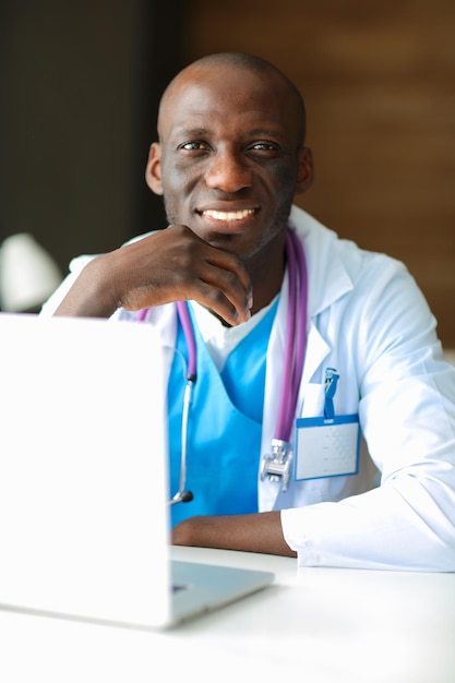 Doctor africano joven que trabaja en la computadora portátil en el escritorio