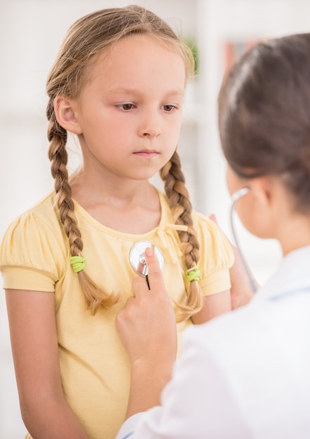 Doctor alegre examen de niña con estetoscopio.