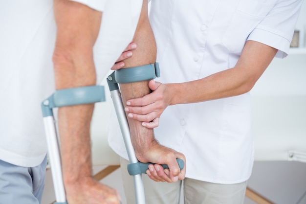 Foto doctor ayudando a su paciente a caminar con muleta