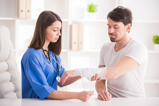 El doctor bastante femenino está vendando el miembro superior del hombre joven.