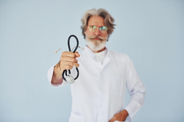 Doctor en bata blanca contra la pared Senior elegante hombre moderno con cabello gris y barba en el interior