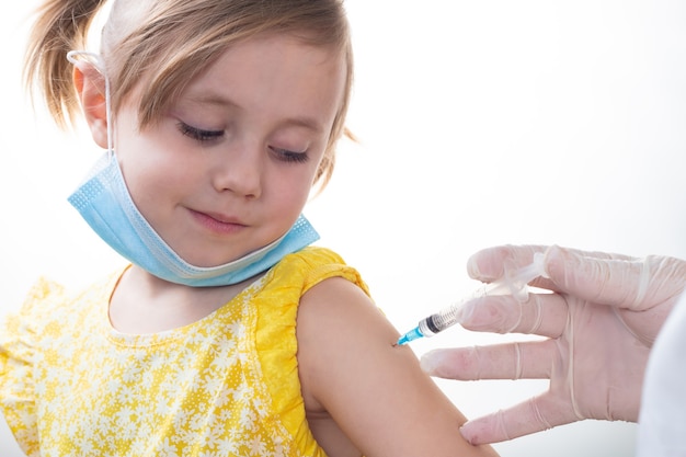 Doctor con bata blanca está vacunando a una joven caucásica con vestido amarillo