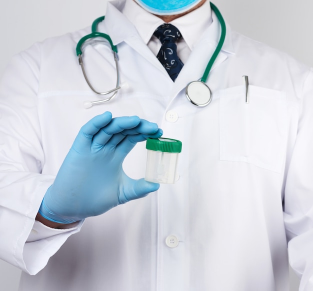 Doctor en bata blanca y guantes de látex estériles azules sostiene un frasco de plástico para el análisis de heces
