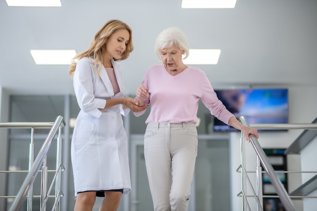 Doctor en una bata de laboratorio ayudando a una mujer en las escaleras