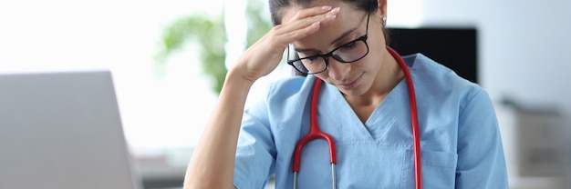 Doctor cansado sentado en la mesa y sosteniendo su cabeza