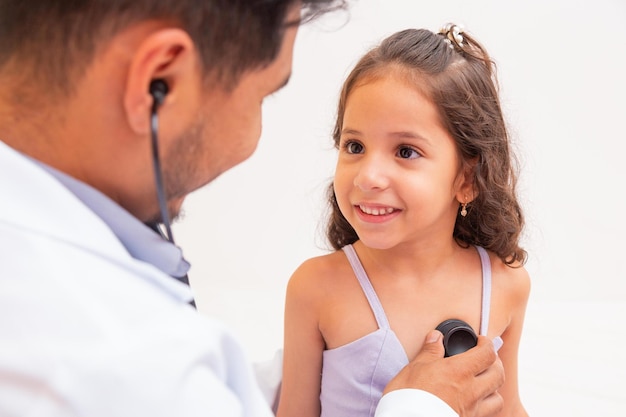 Doctor cariñoso examinando a una chica en la oficina. Doctor examinando el pulmón y el corazón de una niña en el cargo.