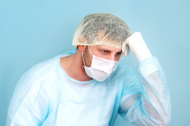 Doctor científico cansado en bata de laboratorio, gorro quirúrgico y máscara se sienta y toma un descanso.