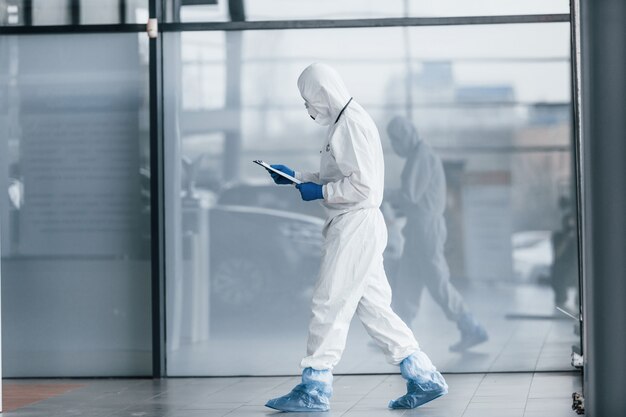 Doctor científico masculino en bata de laboratorio, gafas defensivas y máscara con bloc de notas en las manos