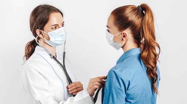 Doctor comprobando la salud de una paciente en máscaras con un estetoscopio sobre un fondo blanco aislado