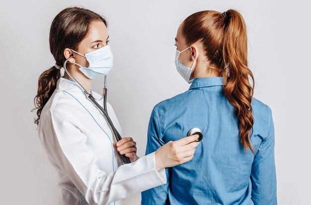 Doctor comprobando la salud de una paciente en máscaras sobre un fondo blanco aislado