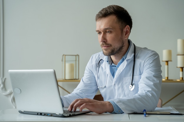 Doctor concentrado trabajando con un portátil en un escritorio en la oficina médico masculino con un portátil en el escritorio en la clínica