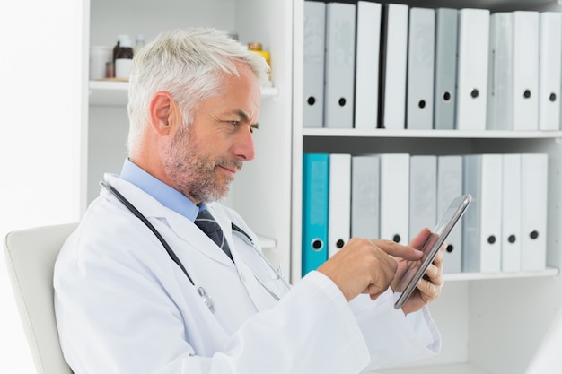 Doctor concentrado usando tableta digital en consultorio médico