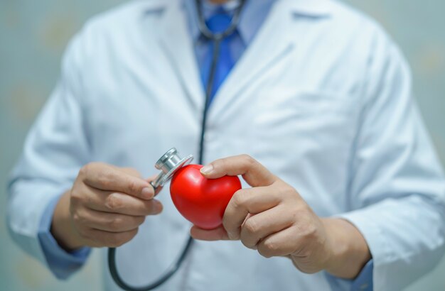 Doctor elegante asiático del hombre que lleva a cabo un corazón rojo