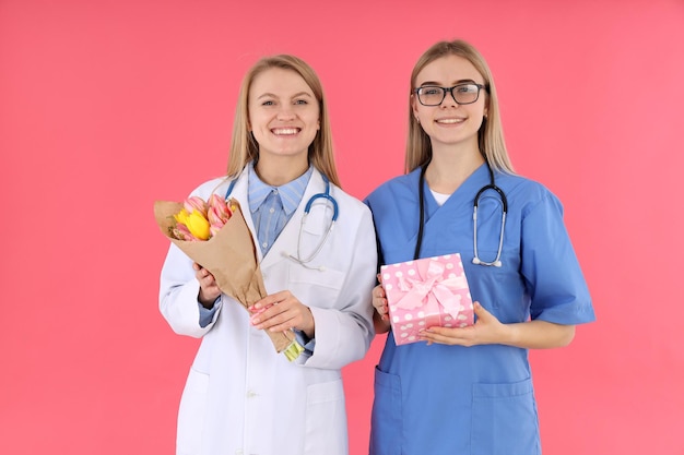 Doctor y enfermera con regalos sobre fondo rosa.