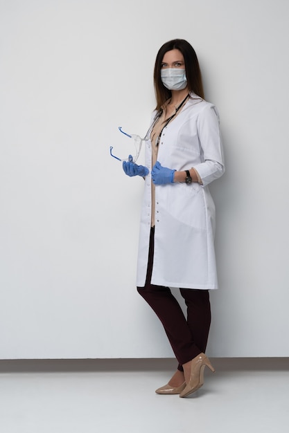 Foto doctor / enfermera sonriendo detrás de la máscara del cirujano. closeup retrato de joven modelo de mujer caucásica en matorral médico blanco y guantes desechables