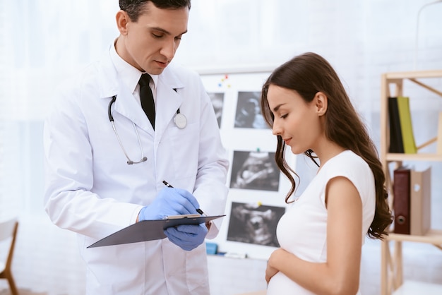 Foto el doctor escribe una receta en papel a una niña embarazada.