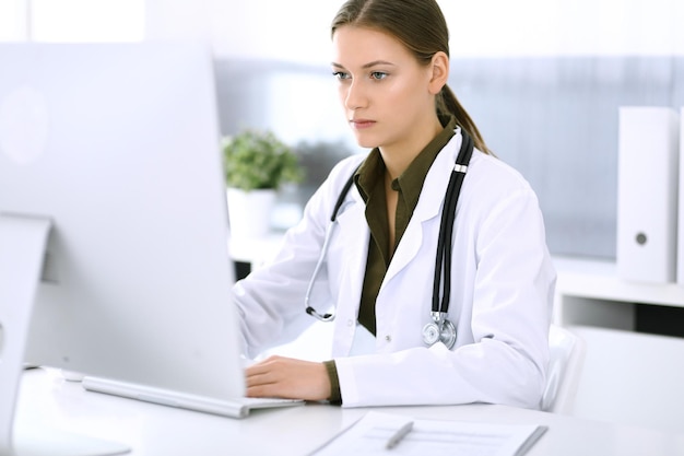 Foto doctor escribiendo en la computadora de la pc mientras está sentado en el escritorio en la oficina del hospital