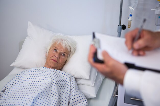 Doctor escribiendo detalles médicos de un paciente mayor