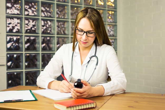 Doctor escribiendo prescripción y sosteniendo la botella con pastillas