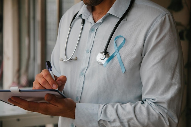 Foto doctor con un estetoscopio en el cuello y una cinta azul escribiendo mes de concientización sobre el cáncer de próstata del hombre