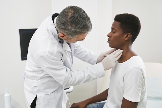 Doctor examinando el cuello del paciente africano.