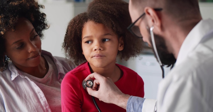 Doctor examinando a una niña afroamericana con un estetoscopio en el consultorio de la clínica