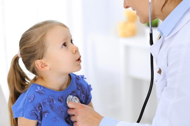 Doctor examinando a una niña con estetoscopio. Paciente niño sonriente feliz en la inspección médica habitual. Conceptos de medicina y salud.