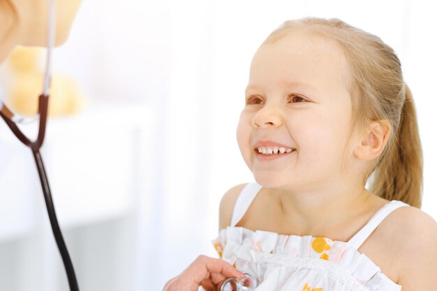 Doctor examinando a una niña con estetoscopio. Paciente niño sonriente feliz en la inspección médica habitual. Conceptos de medicina y salud