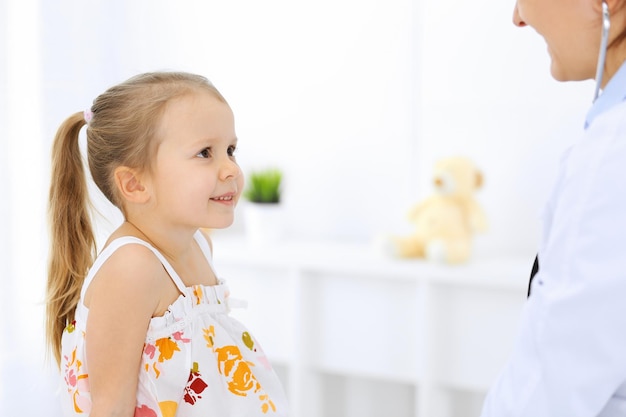 Doctor examinando a una niña con estetoscopio. Paciente niño sonriente feliz en la inspección médica habitual. Conceptos de medicina y salud.