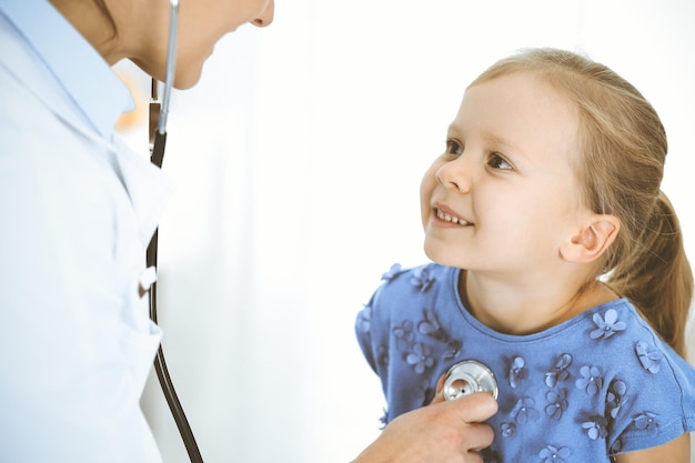 Doctor examinando a una niña con estetoscopio. Paciente niño sonriente feliz en la inspección médica habitual. Conceptos de medicina y salud.