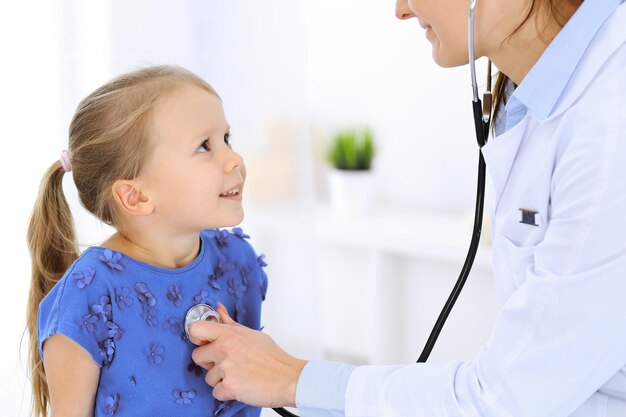 Doctor examinando a una niña con estetoscopio. Paciente niño sonriente feliz en la inspección médica habitual. Conceptos de medicina y salud.