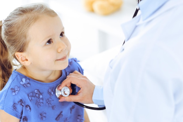 Doctor examinando a una niña con estetoscopio. Paciente niño sonriente feliz en la inspección médica habitual. Conceptos de medicina y salud.