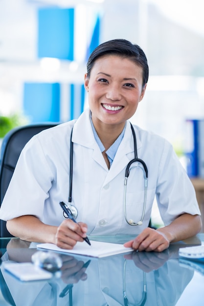 Doctor feliz escribiendo en un cuaderno y sonriendo a la cámara