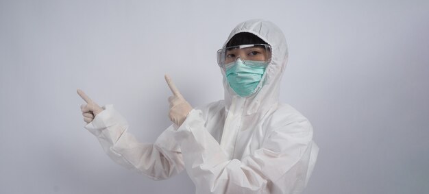 Doctor gesto médico mujer asiática en traje de PPE o equipo de protección personal gesticulando y señalando. guantes de goma médicos blancos. gafas protectoras y máscara verde N95 para proteger el coronavirus pandémico.