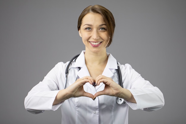 Doctor en gris muestra corazón con sus manos y sonrisas