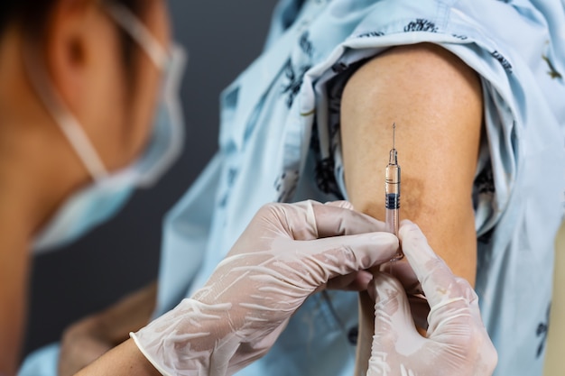 Doctor en guantes con jeringa y haciendo inyección al paciente en máscara médica