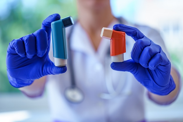 Doctor en guantes médicos de goma azul sostiene inhaladores de asma para pacientes asmáticos durante la consulta médica y el examen. Asistencia sanitaria y tratamiento del asma