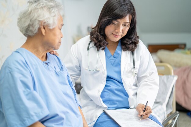 Doctor hablando de diagnóstico y nota en el portapapeles con anciana asiática mayor o anciana mientras está acostado en la cama en la sala del hospital de enfermería, concepto médico fuerte y saludable.