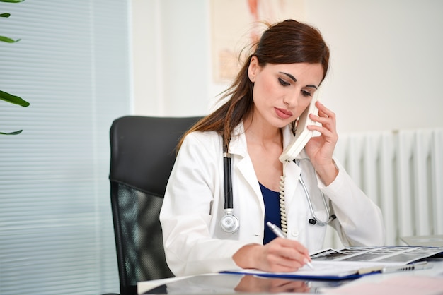 Foto doctor hablando por teléfono en su oficina mientras escribe en un documento