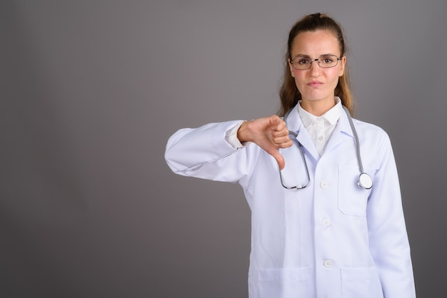 Doctor hermoso joven de la mujer contra fondo gris